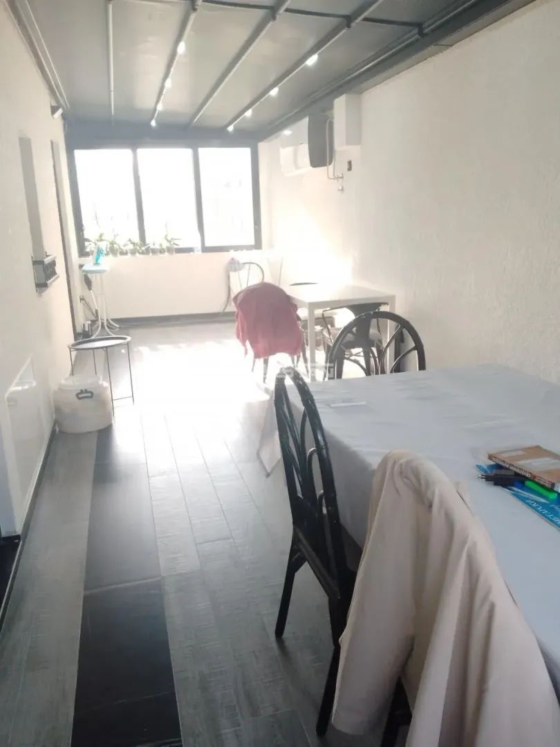 Zastakljena terasa sa trpezarijskim stolom i stolicama.