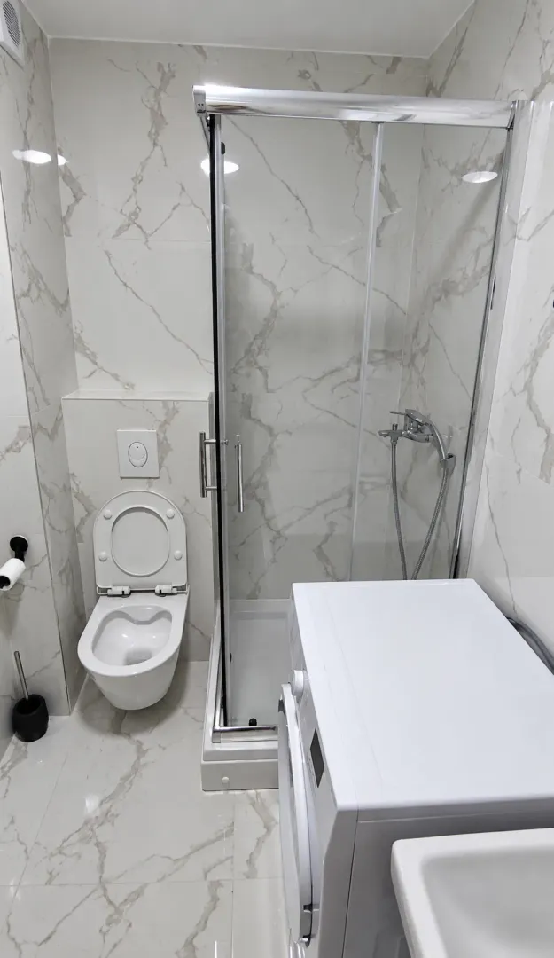Modern bathroom equipped with a shower cabin, toilet, and washing machine.