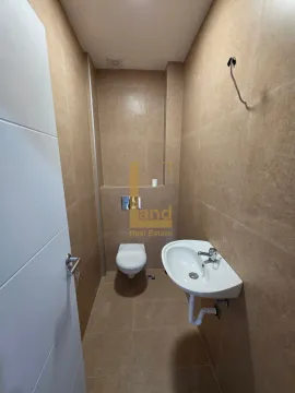 Manje kupatilo sa umivaonikom i toalet šoljom, obloženo bež pločicama. - image 9