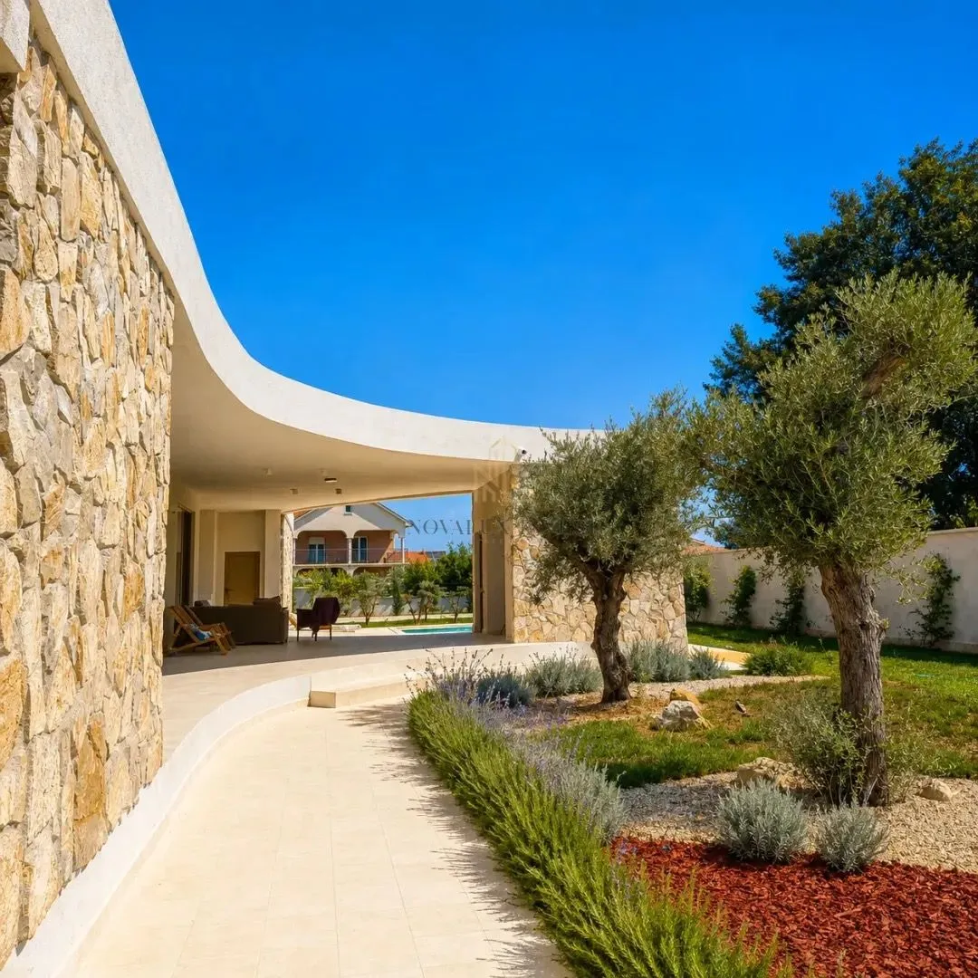 Yard with landscaped garden and terrace in front of a modern stone-clad villa.
