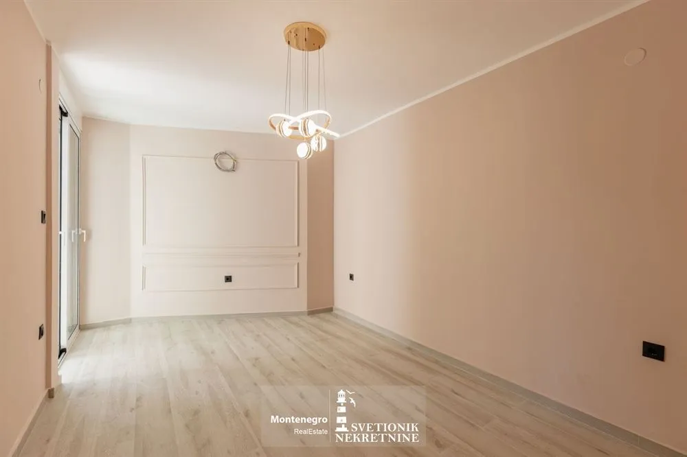 Prazna svijetla soba sa parketom na podu i modernim lusterom.