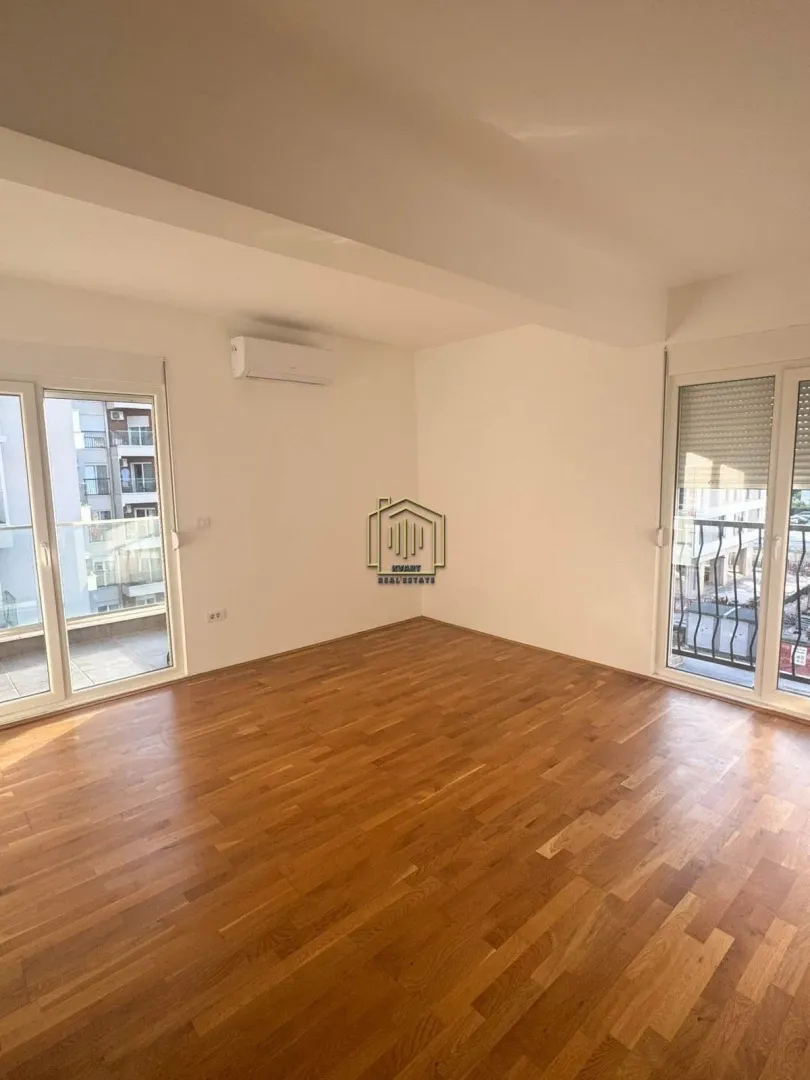 Prazna soba sa parketom i izlazom na balkon.