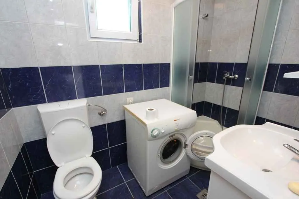 Jednostavno kupatilo sa tuš kabinom, veš mašinom i plavim pločicama.