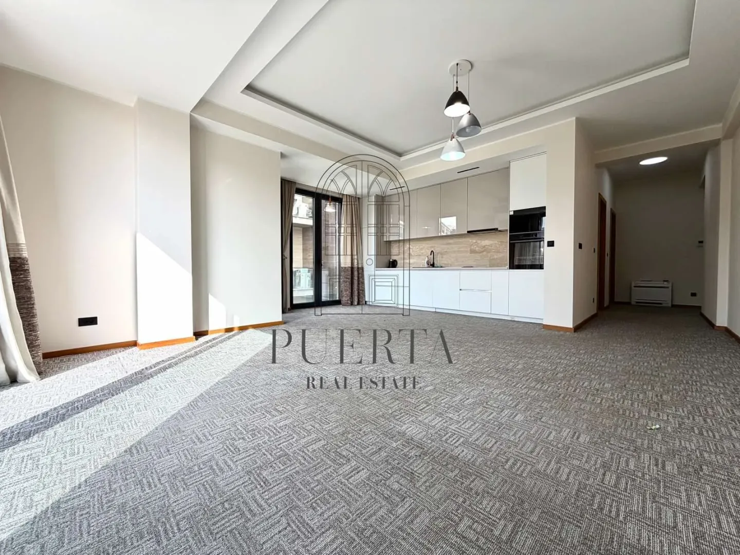 Spacious living room with a kitchen and carpeted floor.