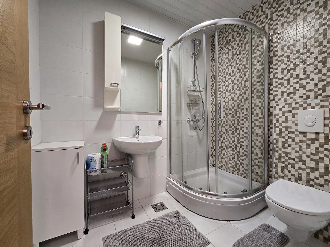 Modernly equipped bathroom with a shower cabin, sink, and toilet.