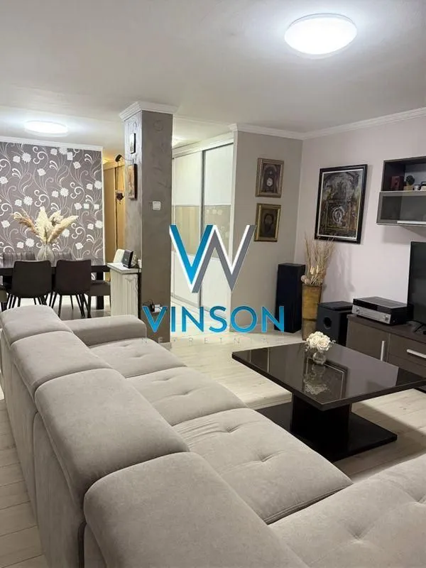 Dnevna soba sa ugaonom garniturom, stočićem i TV komodom.