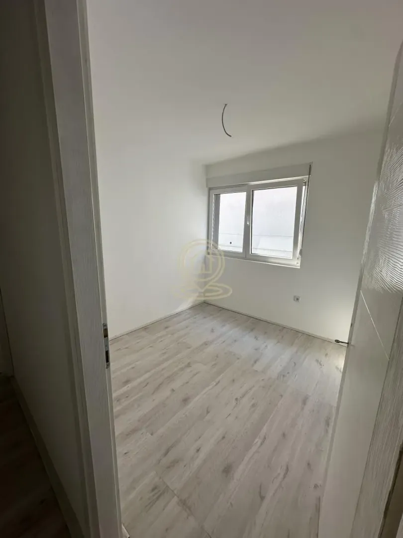 Prazna soba sa laminatom i prozorom, uslikana sa vrata.