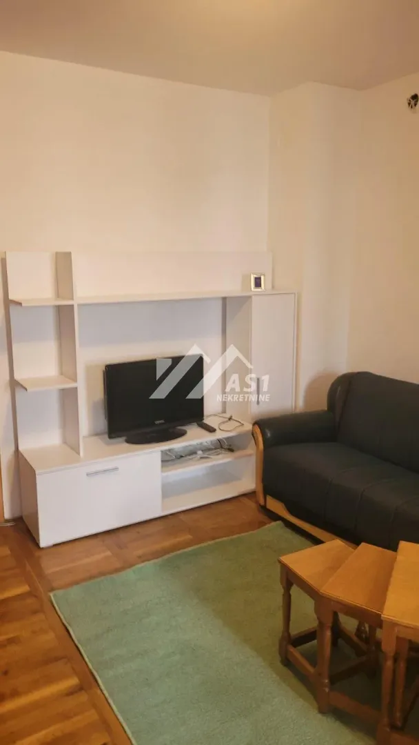Dnevna soba sa garniturom, televizorom i drvenim stolićem.