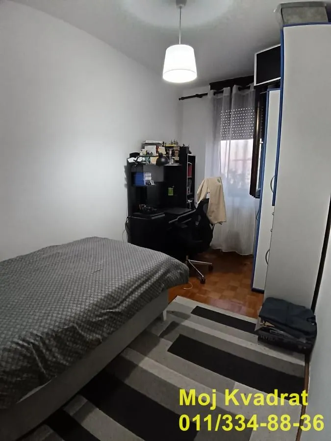Nameštena spavaća soba sa krevetom, radnim stolom i ormarom.