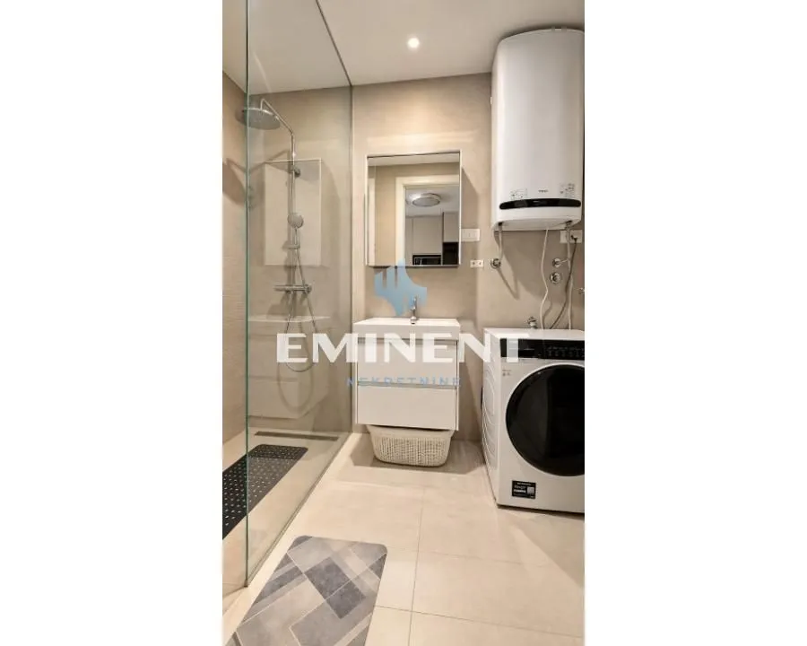 Modern bathroom with a walk-in shower, washbasin, and washing machine.