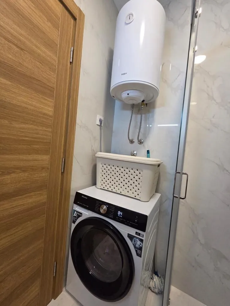 Bathroom with a washing machine, water heater, and shower cabin.