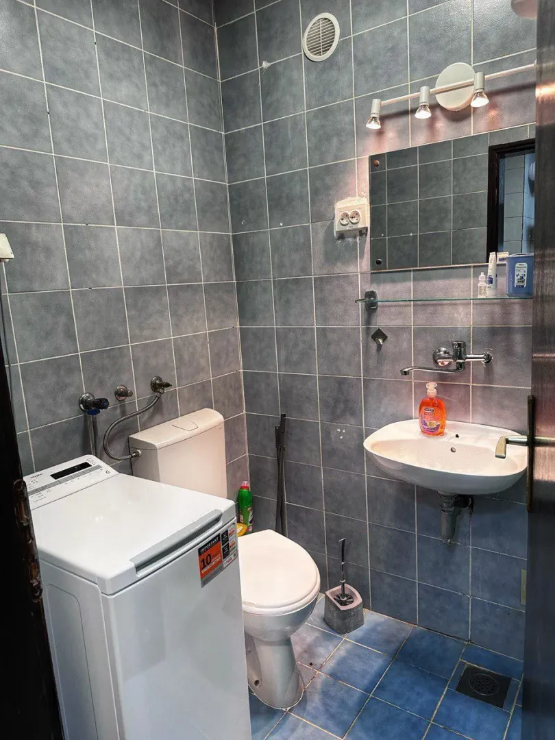 Smaller tiled bathroom with a sink, toilet, and washing machine.