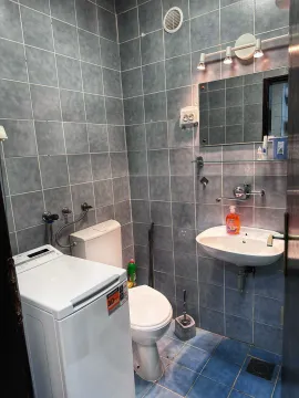 Smaller tiled bathroom with a sink, toilet, and washing machine. - image 5