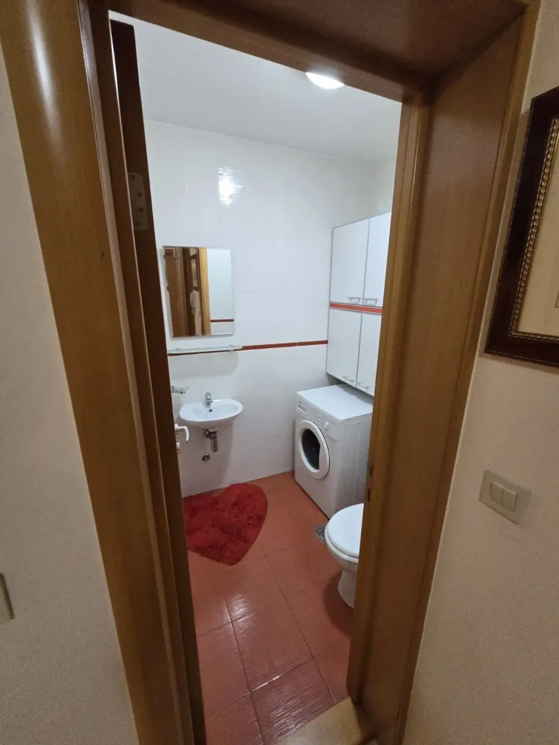 Small bathroom with a washing machine and red tiles, viewed through a doorway.