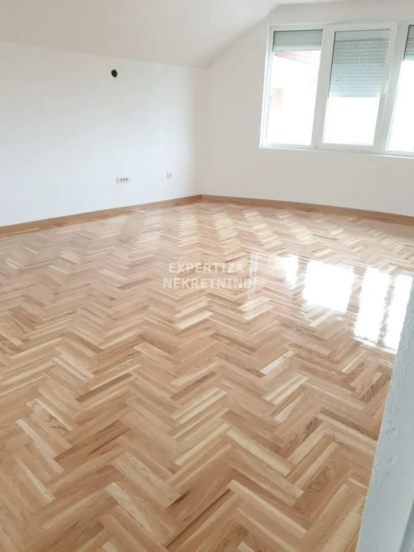Empty room with parquet flooring and a large window.
