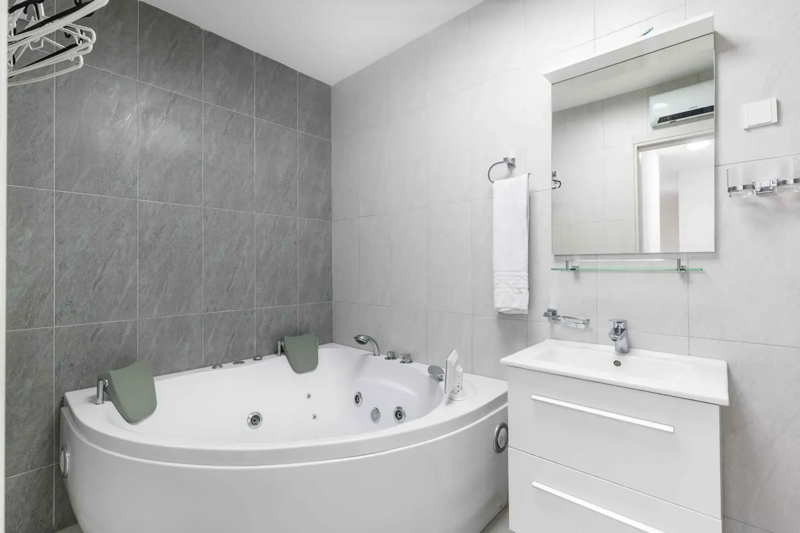 Modernly equipped bathroom with a corner hydro-massage bathtub and a vanity unit.