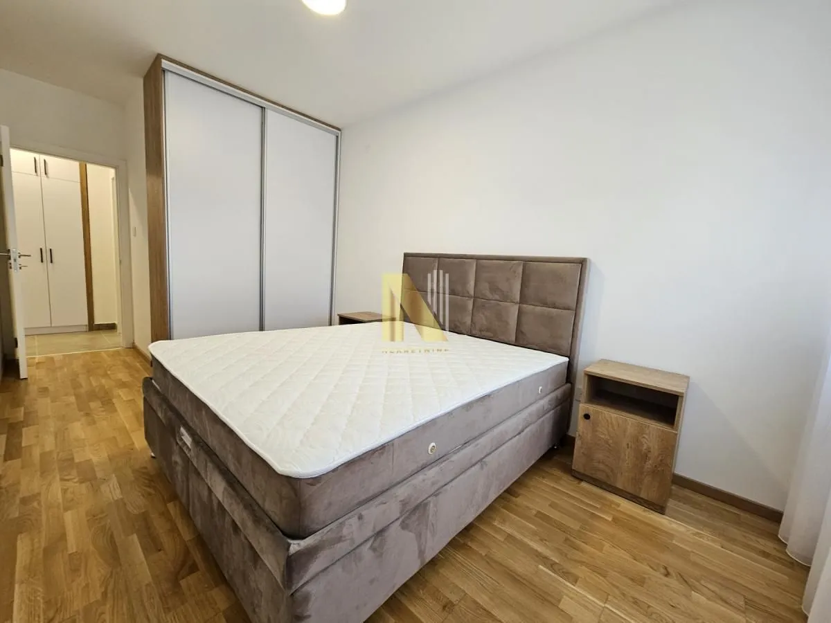 Nameštena spavaća soba sa bračnim krevetom, plakarom i drvenim podom.