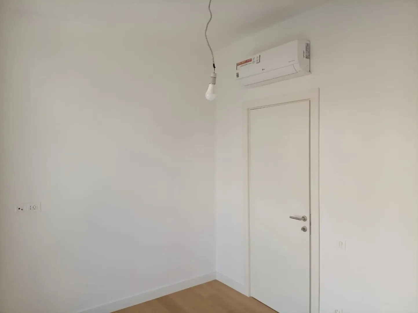 Prazna bijela soba sa drvenim podom, klima-uređajem i vratima.
