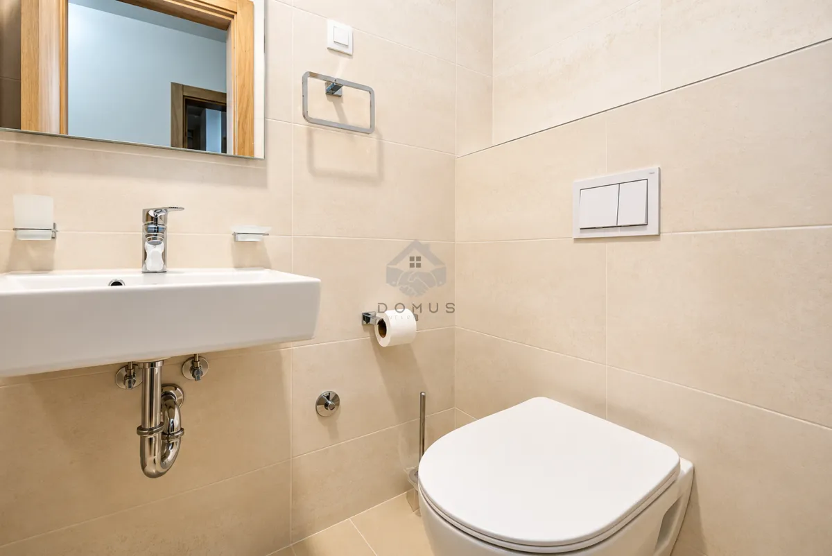 Bathroom equipped with a washbasin, mirror, and toilet featuring beige tiles.