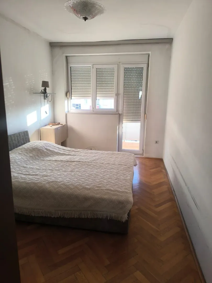 Spavaća soba sa bračnim krevetom, parketom i izlazom na terasu.