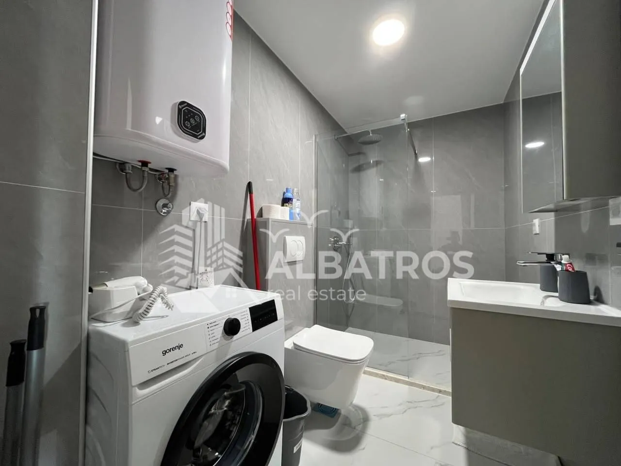 Modern bathroom with a walk-in shower, washbasin, toilet, and washing machine.