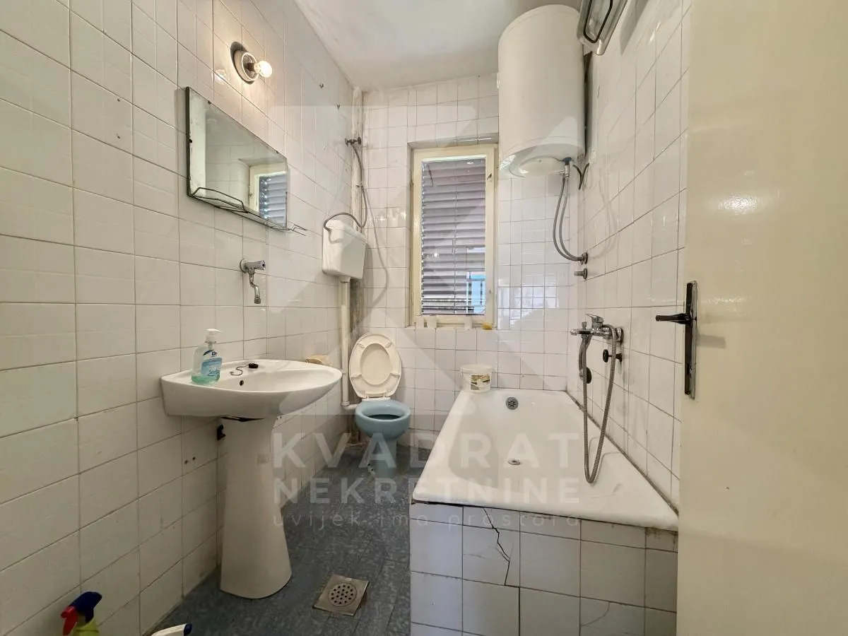 Manje kupatilo obloženo bijelim pločicama sa kadom, umivaonikom i wc šoljom.