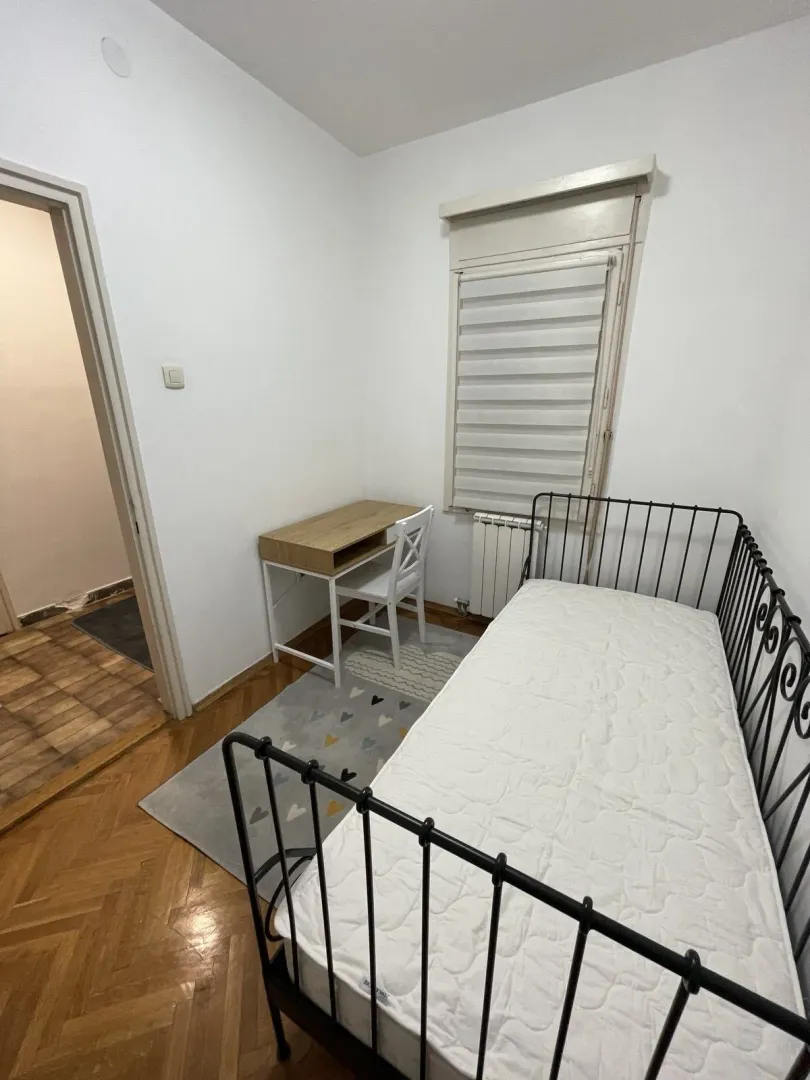 Svijetla spavaća soba sa metalnim krevetom i radnim stolom.
