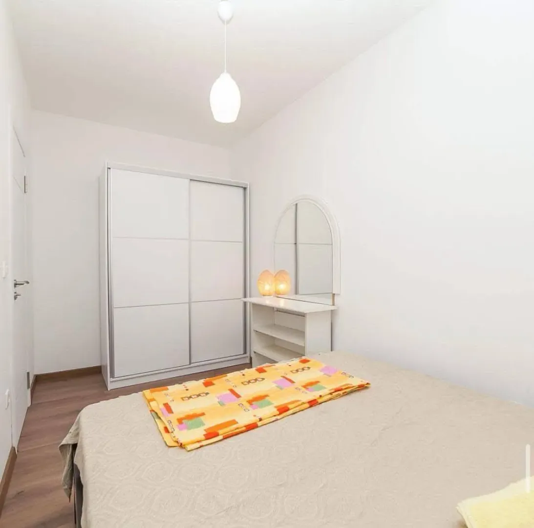 Bright bedroom with a double bed, white wardrobe, and a dresser with a mirror.