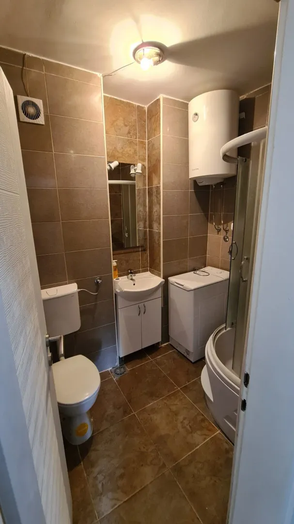 Small bathroom with a shower cabin, washbasin, toilet, washing machine, and water heater.