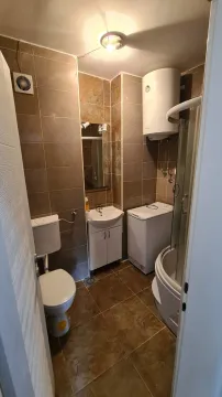 Small bathroom with a shower cabin, washbasin, toilet, washing machine, and water heater. - image 6
