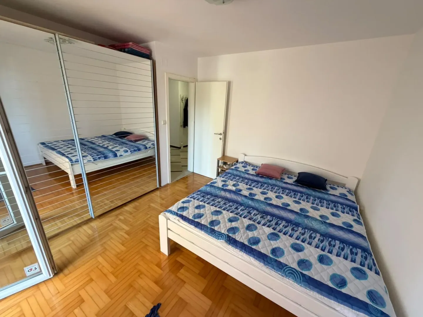 Spavaća soba sa bračnim krevetom i velikim ormarom sa ogledalom.