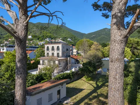 Pogled na vilu sa kamenom fasadom i dvorište okruženo zelenilom i planinama. - image 4