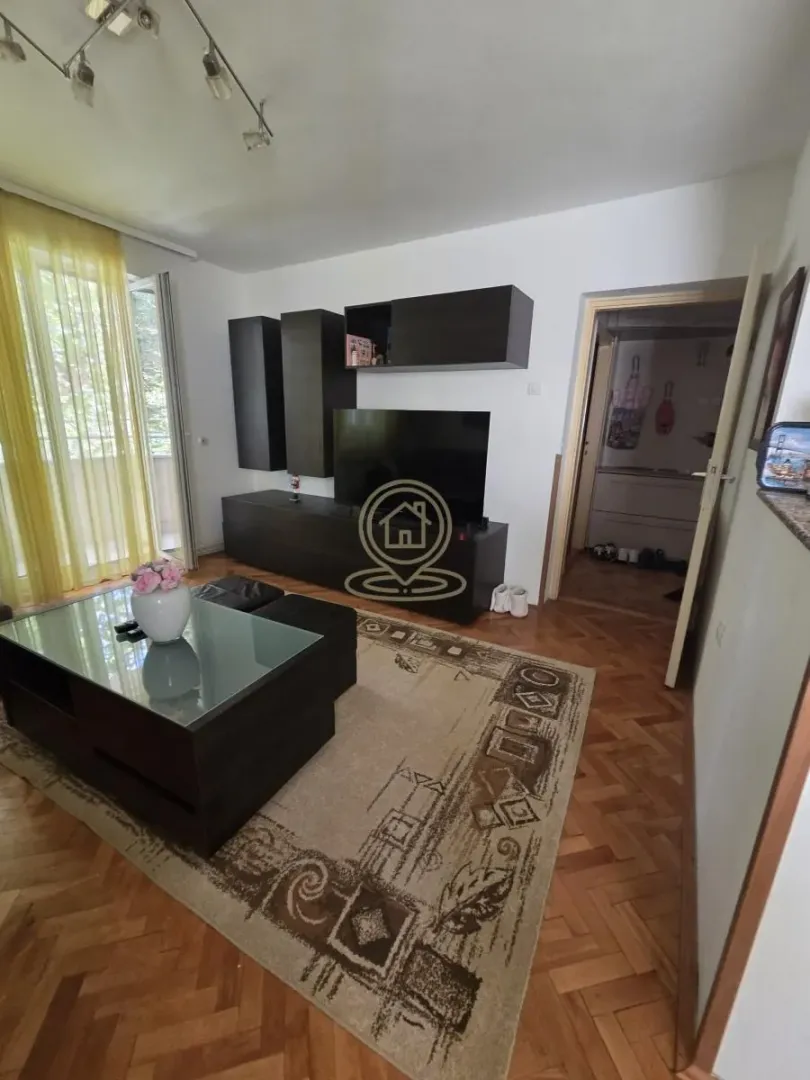 Dnevna soba sa garniturom, televizorom i izlazom na balkon.