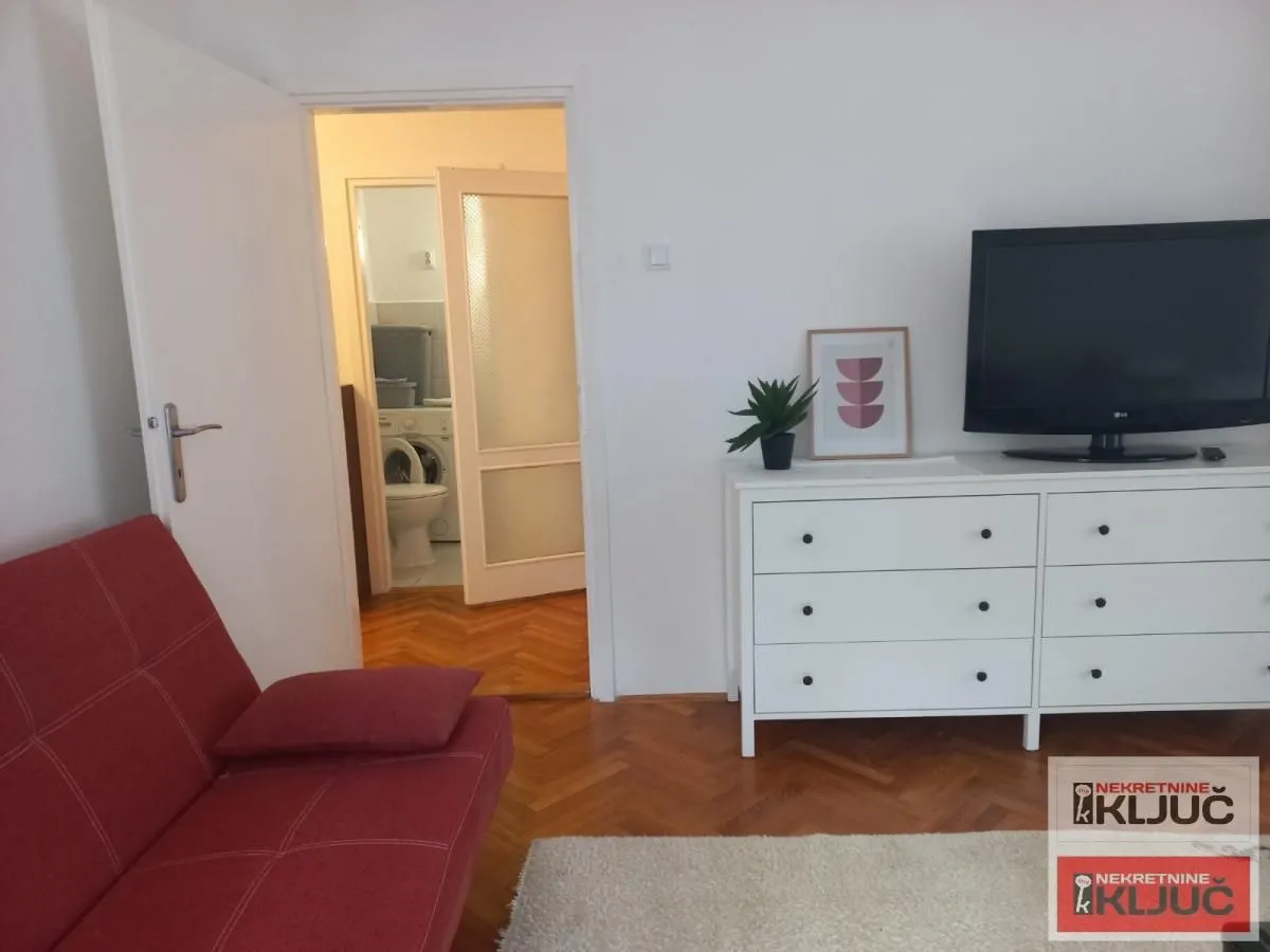 Dnevna soba sa crvenim kaučem, komodom i televizorom.