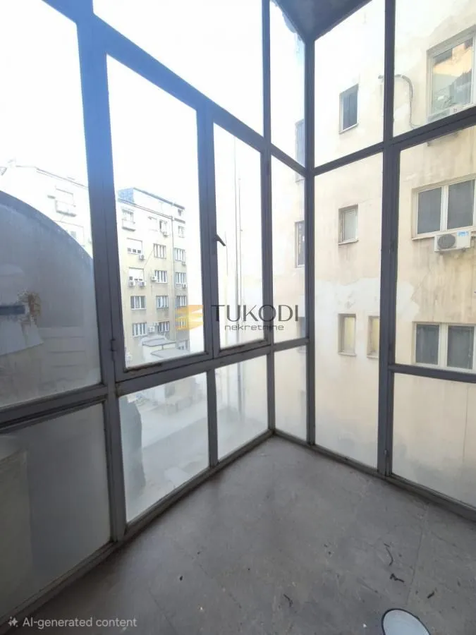 Zastakljeni balkon sa velikim staklenim površinama i pogledom na okolne zgrade.