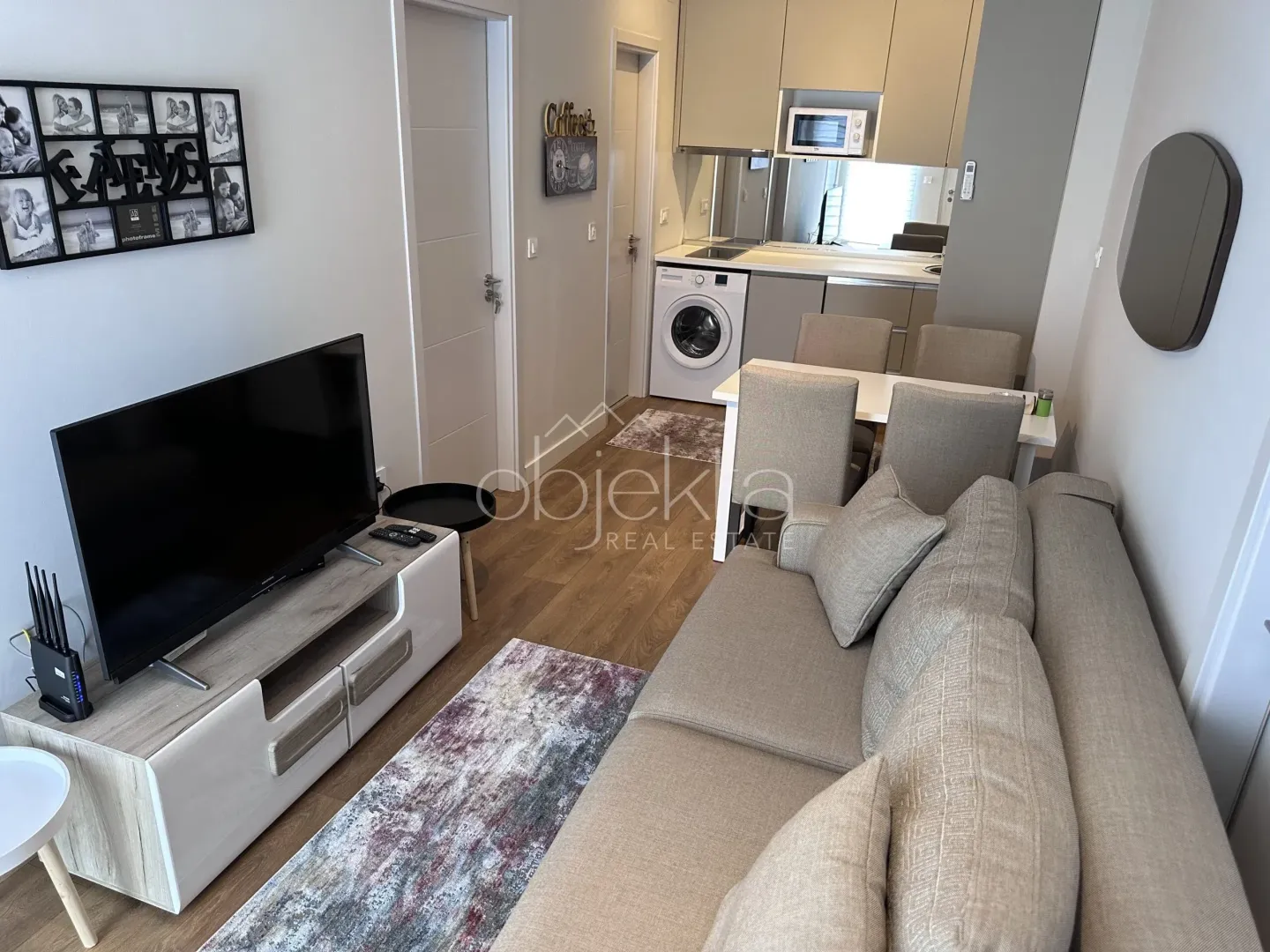 Living room with sofa, TV and kitchen in the background.