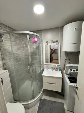 Small bathroom with a shower cabin, washbasin, and washing machine. - image 6