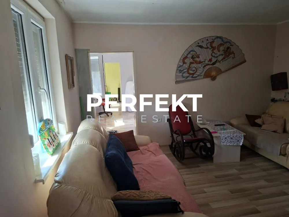 Dnevna soba sa sofom, foteljom i dekorativnim lepezama na zidu.