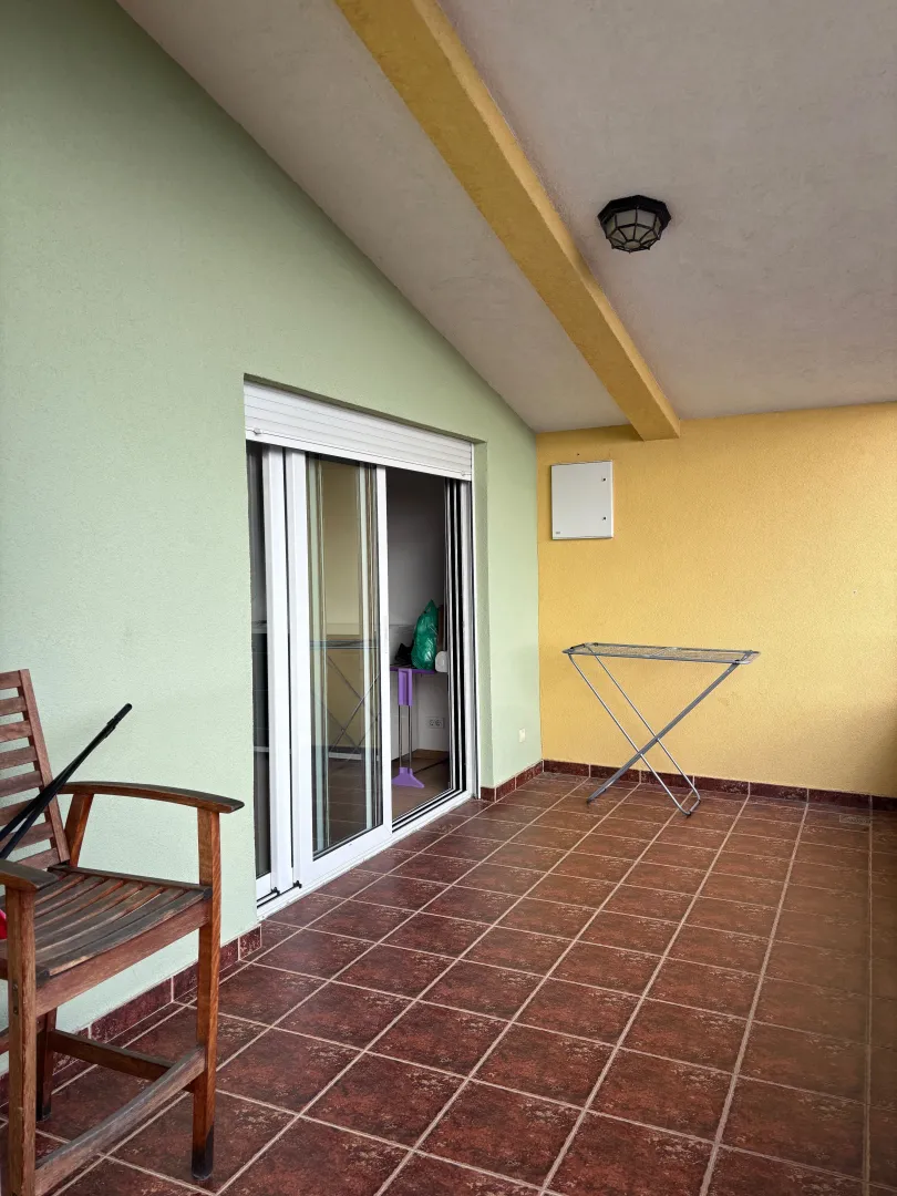 Covered terrace with ceramic tiles and a wooden chair.