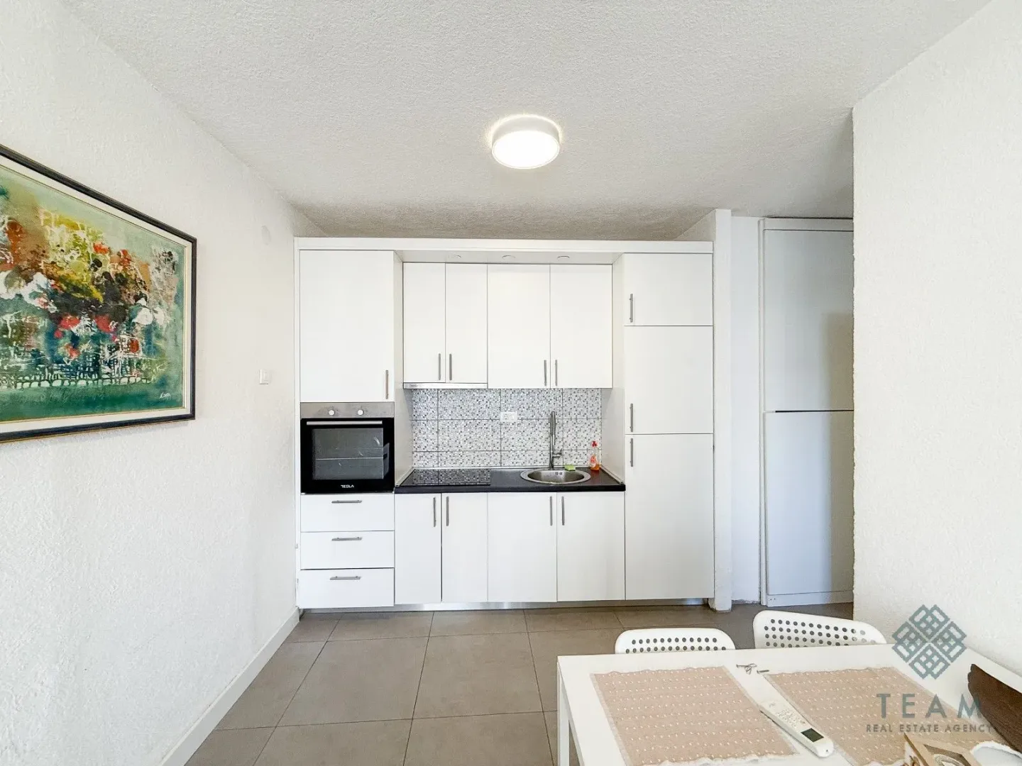 Small white kitchen with built-in appliances and a dining table in the foreground.
