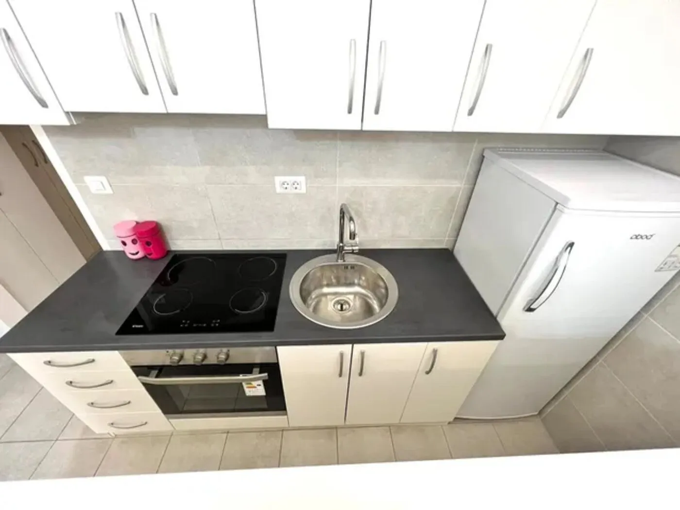 Small kitchen with white cabinets, built-in cooktop, and a refrigerator.