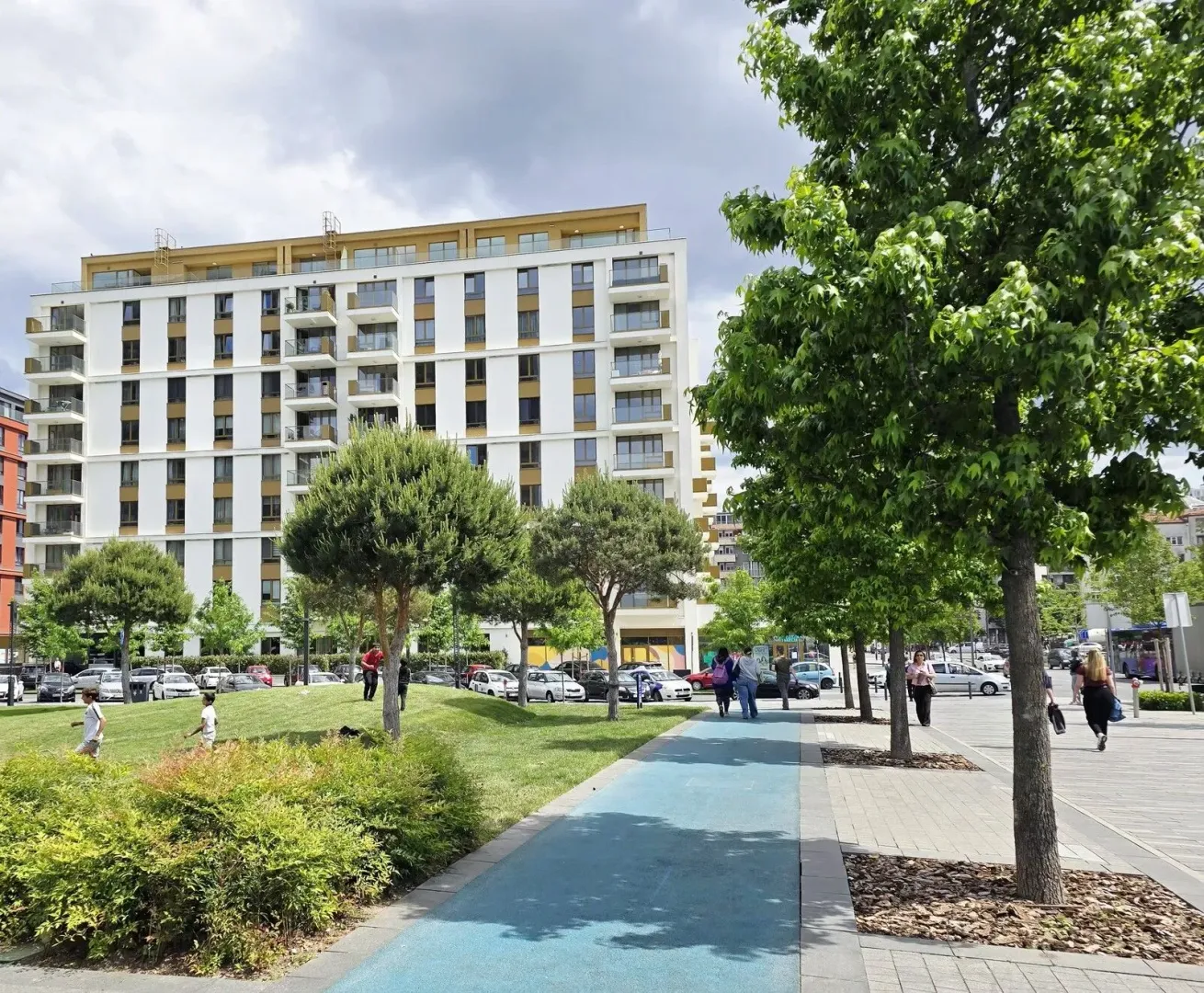 Pogled na modernu stambenu zgradu sa uređenom zelenom površinom i šetalištem.