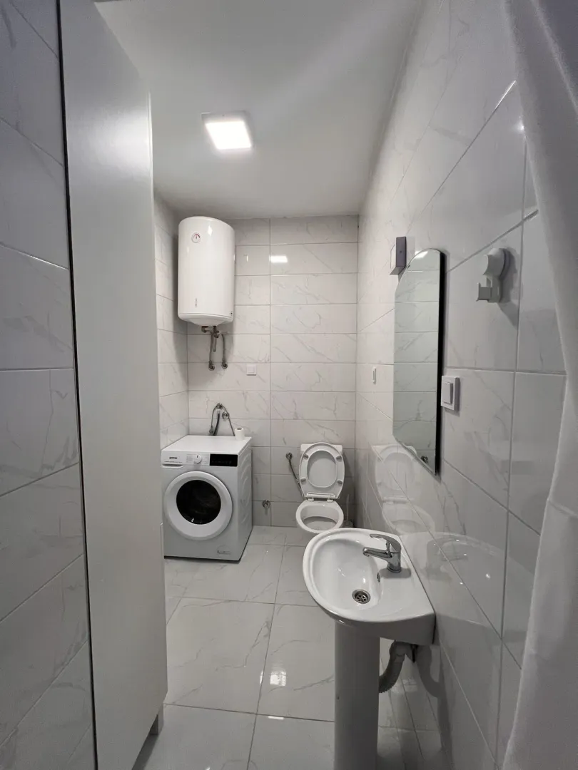 Svijetlo kupatilo sa veš mašinom, bojlerom i sanitarijama.