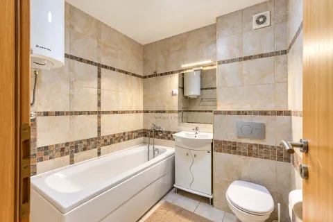 Bathroom equipped with a bathtub, washbasin, and toilet, tiled in beige. - image 10