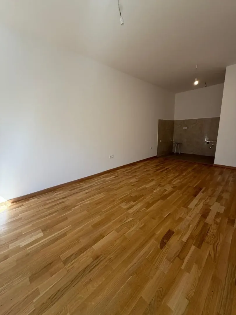 Prazna prostorija sa drvenim podom i bijelim zidovima.