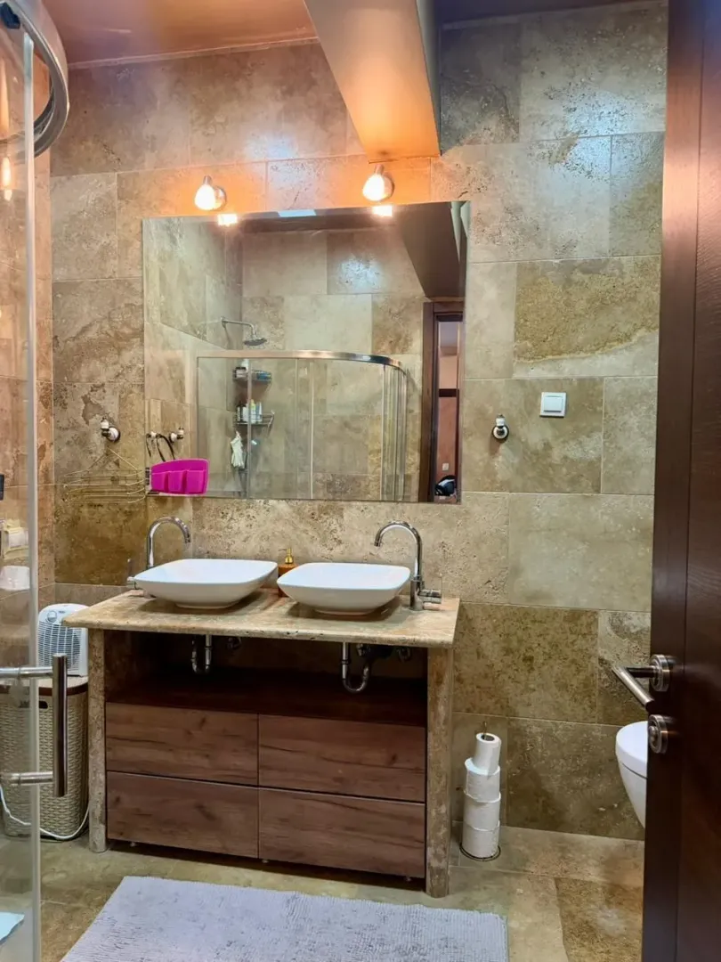 Modern bathroom with dual sinks and stone-patterned ceramic tiles.