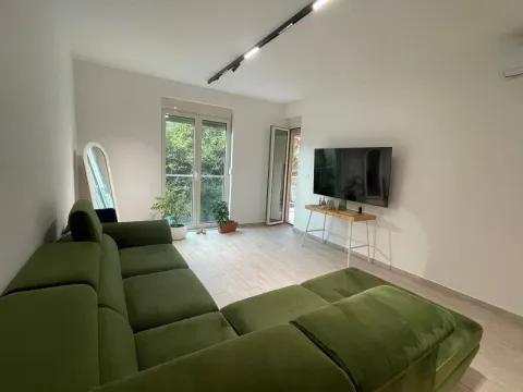 Dnevna soba sa zelenom ugaonom garniturom, televizorom i izlazom na terasu. - image 3