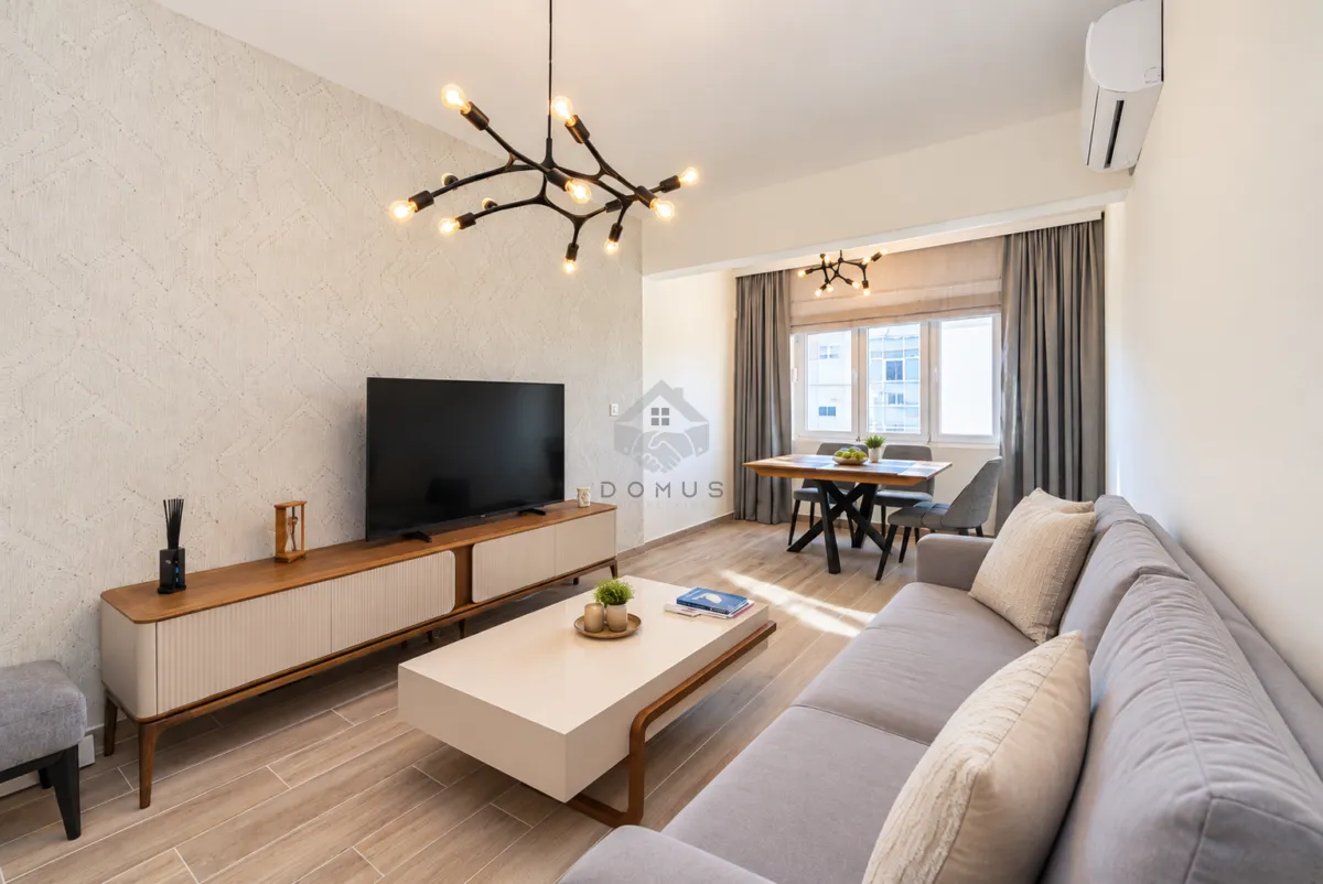 Spacious living room with sofa, TV, and dining area in the background.