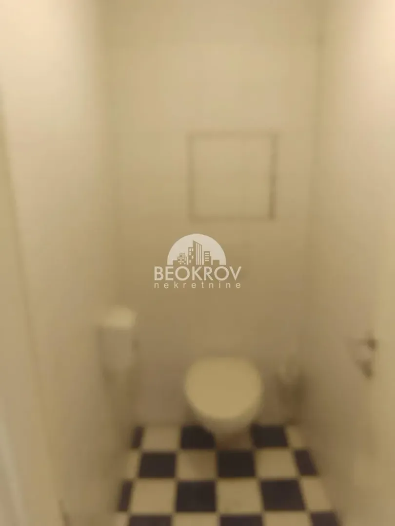 Manje kupatilo sa WC šoljom i pločicama sa šahovskim uzorkom na podu.