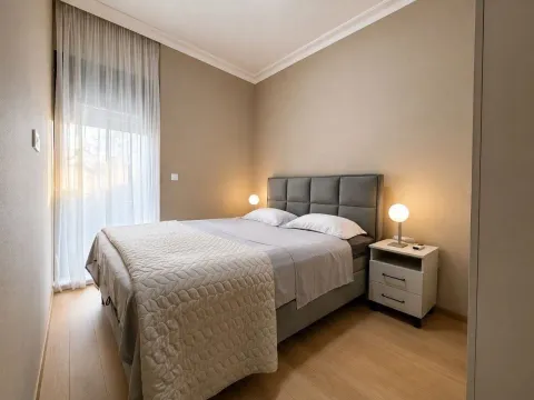 Uređena spavaća soba sa bračnim krevetom, noćnim stočićem i prozorom sa bijelom zavjesom. - image 3